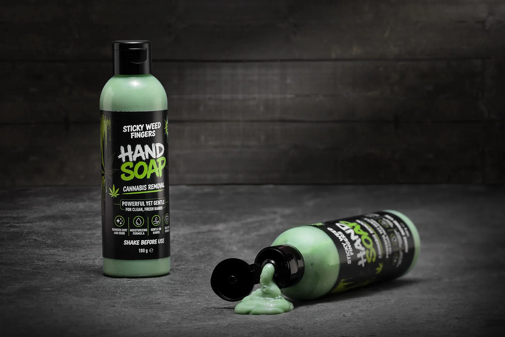 Two bottles of Sticky Weed Fingers Hand Soap on dark concrete — one lying down, pouring soap out